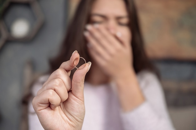 Frustrated young woman holding ring in hand, crying