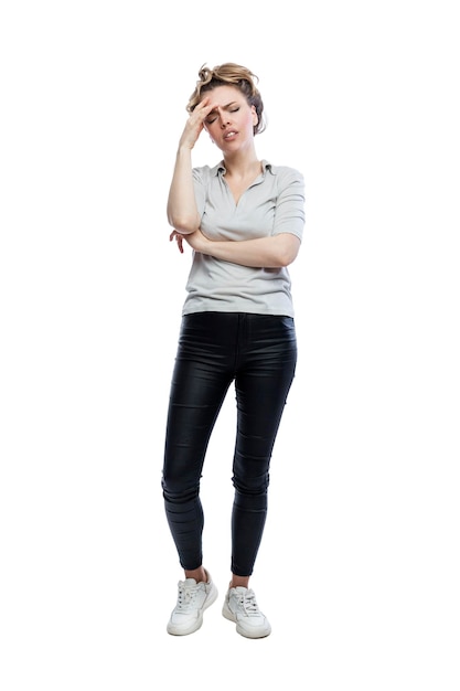 A frustrated young woman is standing Beautiful blonde in black leggings a gray tshirt and white sneakers Stress depression and negativity Full height Isolated on white background Vertical