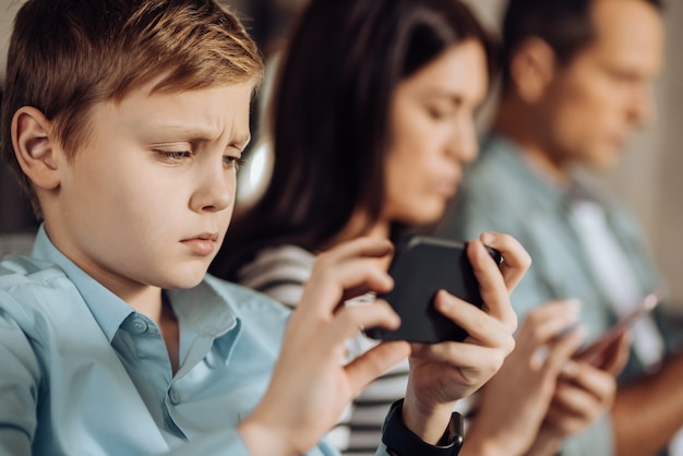 Frustrating result. Cute little boy pouting and being disappointed about the result of the game while his parents using their phones in the background