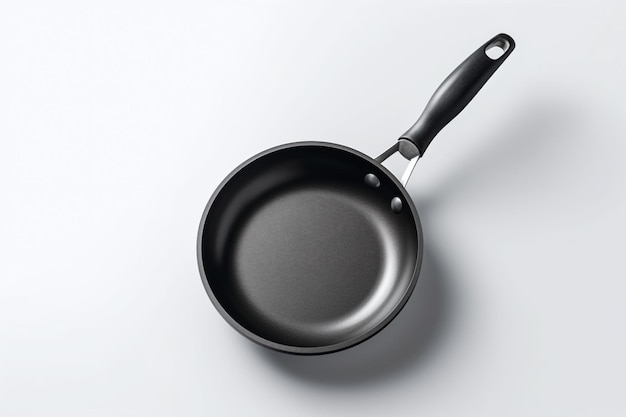 A frying pan with a black handle sits on a white surface.