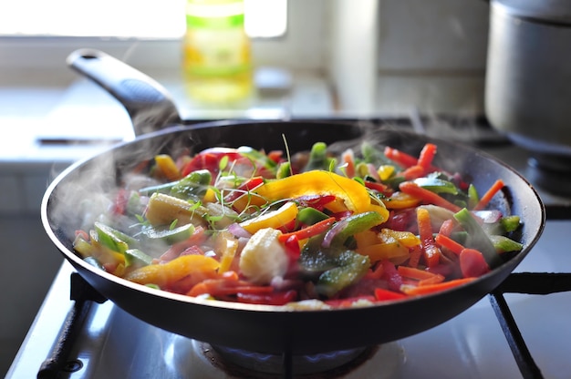 Frying pan with colorful peppers and herbs on the gas stove