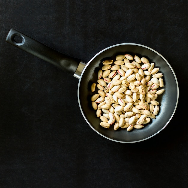 Frying pan with pistachios on a black background. 