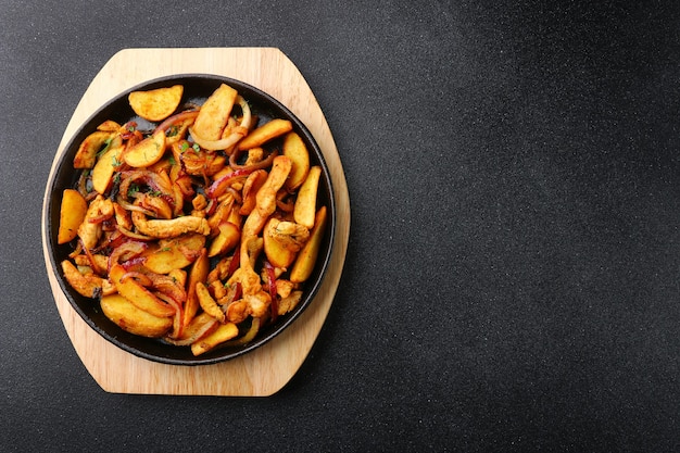 Frying pan with potatoes meat and roast onion on black concrete background  