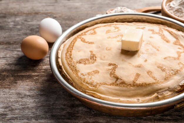 Frying pan with thin pancakes and butter on table