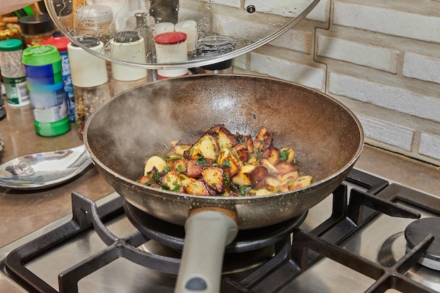 Frying pans with fried potatoes and parsley with an open lid and steam on gas stove in the kitchen Step by step recipe