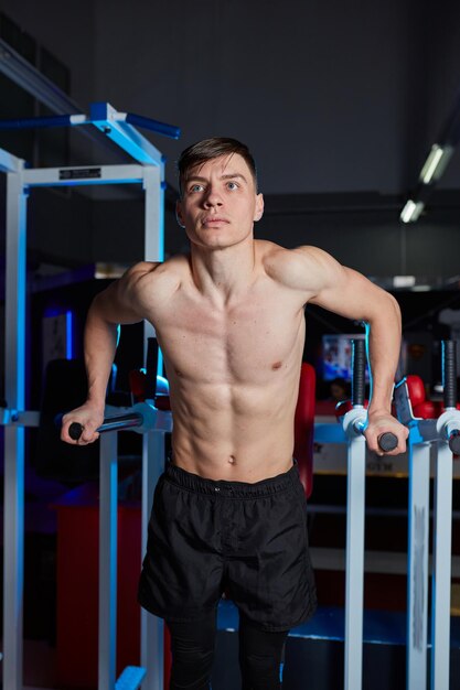 Ftness sport and people concept young man doing triceps exercise diving on uneven bars in the gym