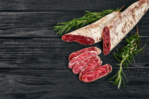 Fuet Salami and Rosemary Traditional Spanish sausage On a black wooden background Top view