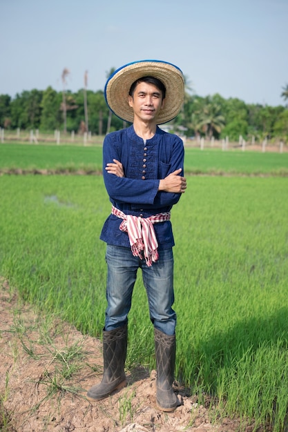 The full body of Asian farmer man wear traditional costume standing and cross arms at a green rice farm