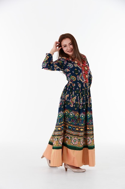 Full body Asian female in authentic ornamental dress holding hand on waist and gesticulating while dancing against white background