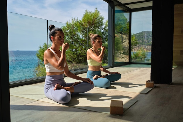 Full body of barefoot females in activewear sitting in Padmasana posture on sports mats on terrace