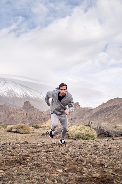 Full body of bearded male in sportswear and sneakers running on stony ground near volcano of Teide in Tenerife in Canary Islands in Spain