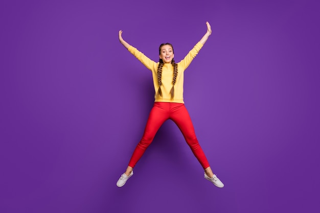 Full body  crazy youngster lady jumping high spending best free time spread hands star shape wear casual yellow pullover red trousers isolated purple color wall