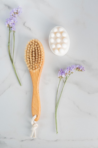 Full body dry massage brush and handmade honey soap from above on marble background with purple flowers