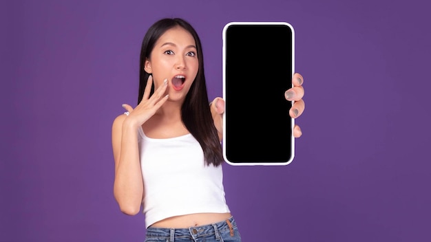 Full body length photo portrait of beautiful Asian young woman Excited surprised girl showing big smart phone with blank screen white screen isolated on purple background Mock Up Image