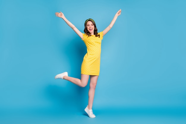 Full body photo of girlish enthusiastic young girl raise hands leg isolated over blue color background