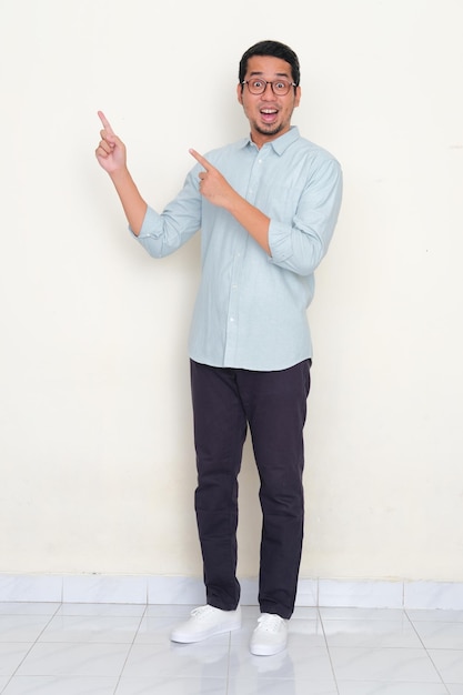 Full body portrait of Asian man pointing to the right side with excited expression