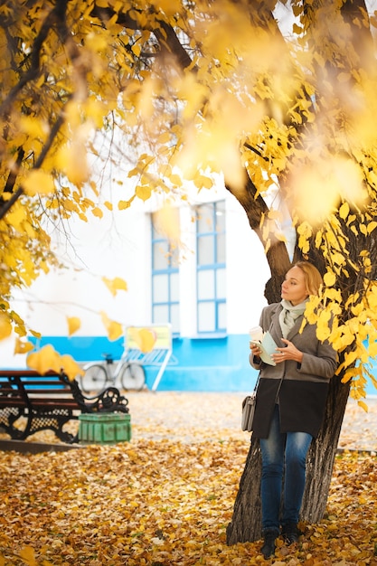 Full body portrait of elegant woman walking with coffee and note in autumn park