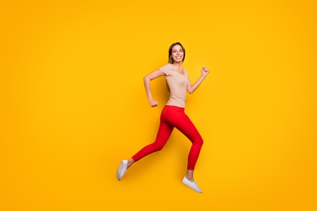 Full body profile photo of funky lady jumping high rushing discount shopping store addicted person wear casual striped t-shirt red trousers isolated yellow color wall