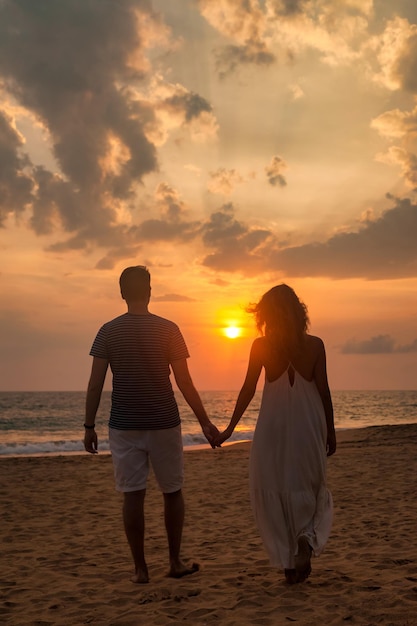 Full body rear view young lovely family couple man and woman in casual clothes holding hands walking together sandy beach at ocean sunset background outdoor