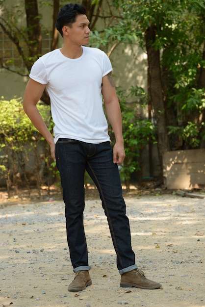 Full body shot of handsome Asian man thinking at the park outdoors