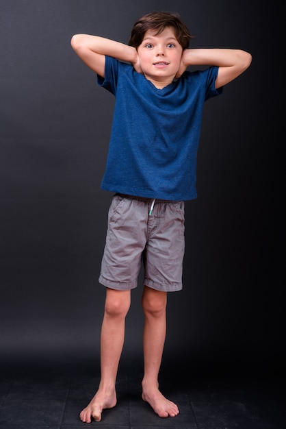 Full body shot of young boy covering ears and looking shocked