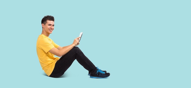 Full body Teenage boy portrait sitting using tablet computer isolated on blue background