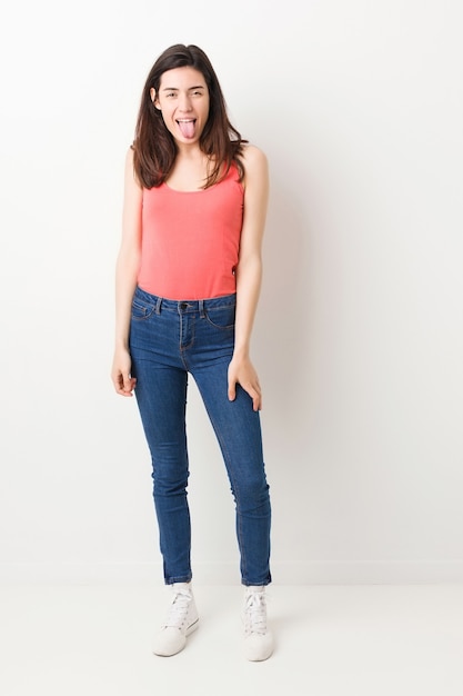 Full body young woman on white background funny and friendly sticking out tongue.