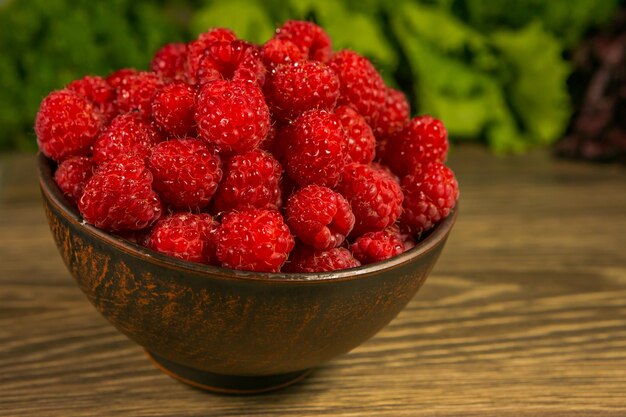 Full bowl of ripe raspberries on a wooden table