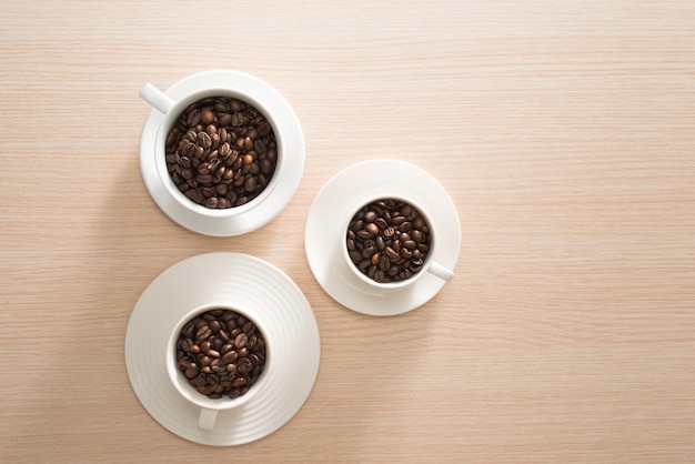 Full coffee beans cups on the wood background