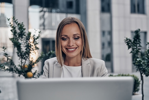 Full concentration at work. Beautiful young woman using laptop and smiling while working indoors