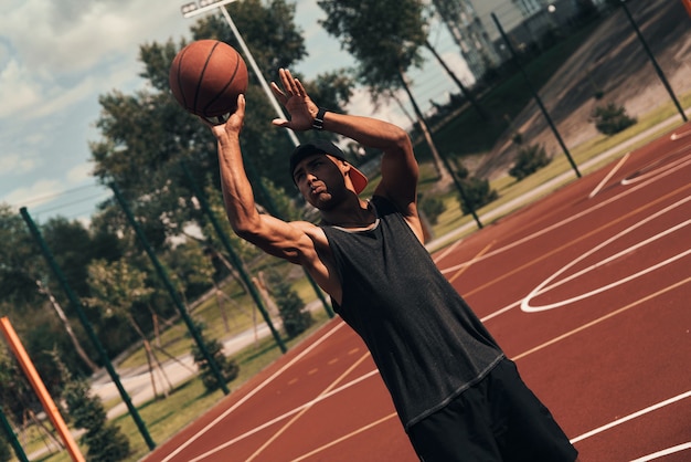 Full of energy. Young African man in sports clothing throwing a ball while playing basketball outdoors