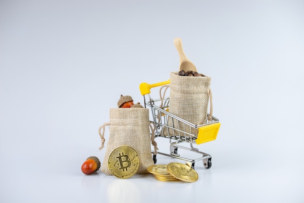 Full filled sack bags with acorns and coffee beans, on a cart, beside golden coins.