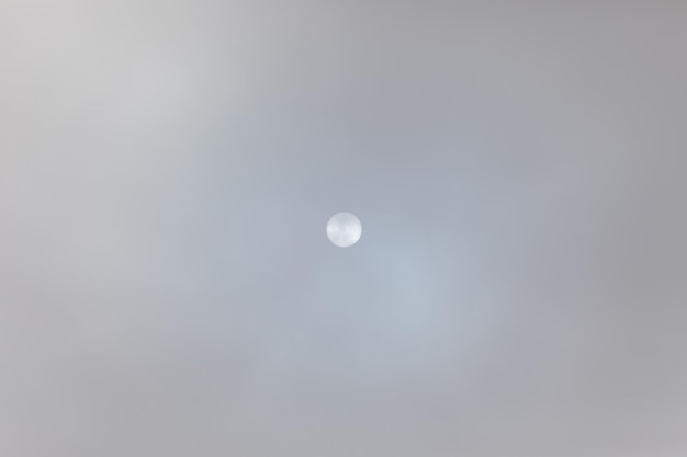 Full frame of unclear sky with midday sun in the middle shinning through a dense grey clouds