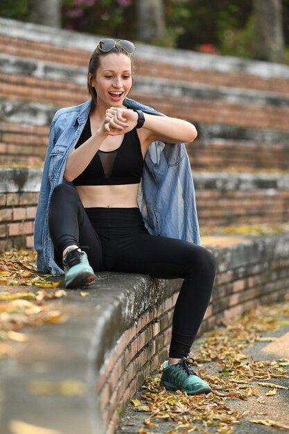 Full length of athletic woman checking fitness results or heart rate on smartwatch after running in the park