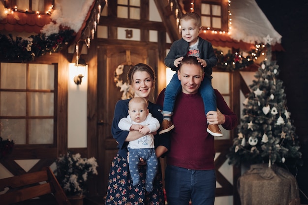 Full length of attractive young Caucasian family with two sons standing in room decorated with artificial snow