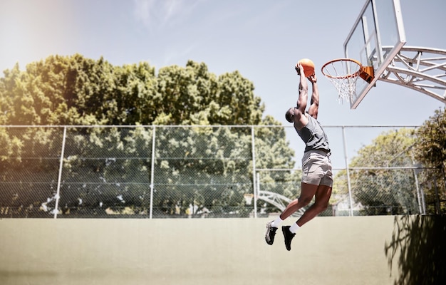 Full length of basketball player dunking a ball into the net during a match on a court Fit and active athlete jumping to score during a competitive game Healthy athletic african man in action