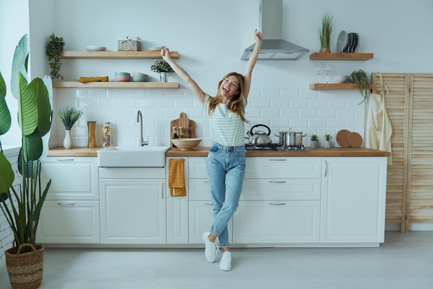 Full length of beautiful young woman looking happy while standing at the domestic kitchen