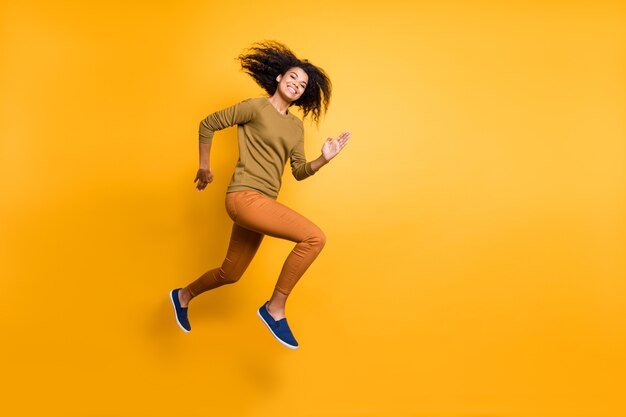 Full length body size photo of cheerful positive beautiful attractive charming pretty girl wearing orange pants trousers running jumping towards empty space isolated over vivid color background