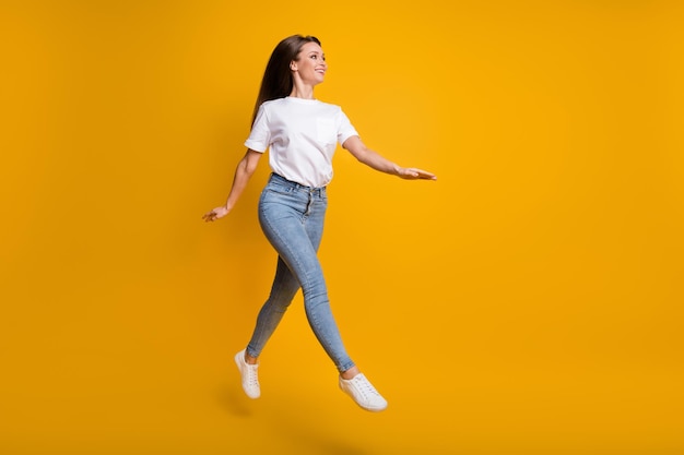 Full length body size photo of girl jumping up walking looking at empty space isolated on bright yellow color background