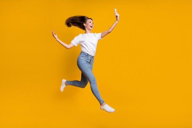 Full length body size photo of pretty woman taking selfie throwing hair jumping up isolated on bright yellow color background