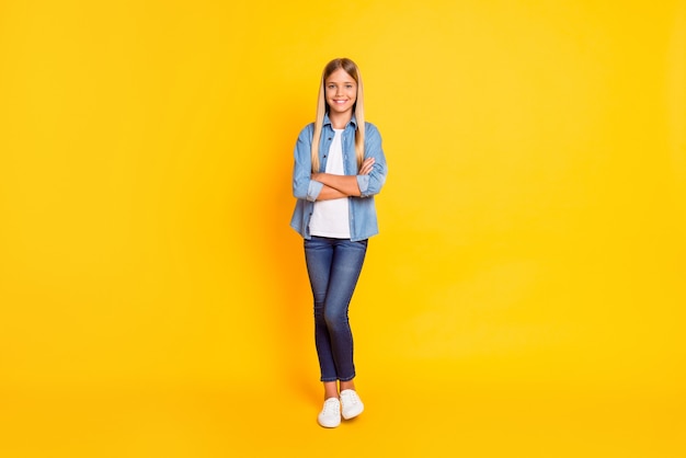 Full length body size photo of schoolgirl with straight blonde hair keeping hands crossed isolated on bright yellow color background