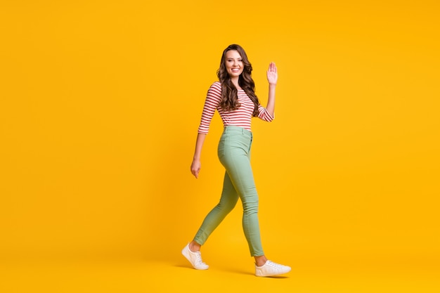 Full length body size side profile photo of girl with hurrying up waving with hand smiling isolated on bright yellow color background