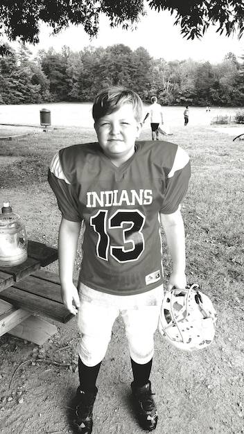 Photo full length of boy in sports clothing holding helmet while standing on field