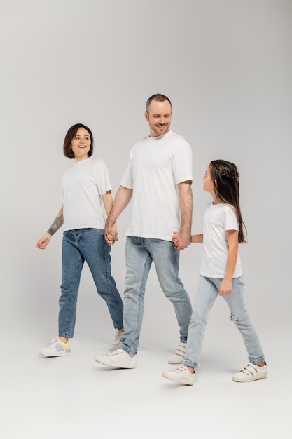 full length of cheerful parents and preteen daughter in white tshirts and blue denim jeans holding