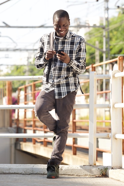 Full length college student standing outside with bag and cell phone