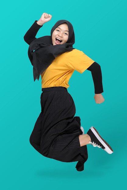 Full length of Cute Asian teenager girl wearing headscarf jumping on blue