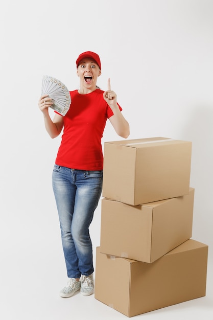 Full length of delivery woman in red cap, t-shirt isolated on white background. Female courier near empty cardboard boxes, bundle of dollars, cash money. Receiving package. Copy space advertisement.