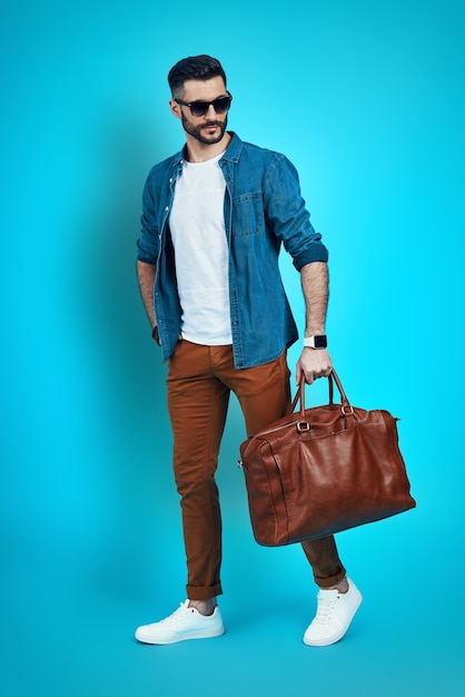 Full length of fashionable young man looking away while walking against blue wall