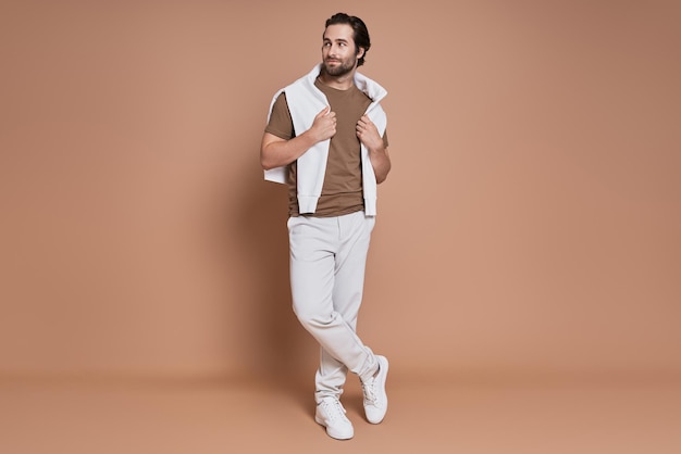 Full length of fashionable young man standing against brown background