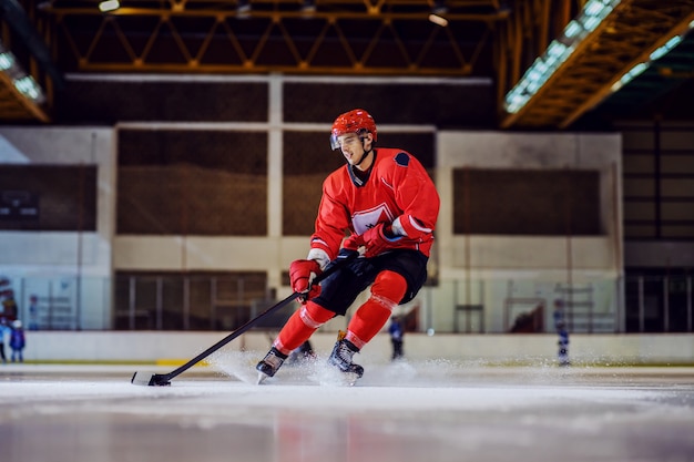 Full length of fearless hockey player skating towards goal and trying to make a score. Hall interior. Winter sports.